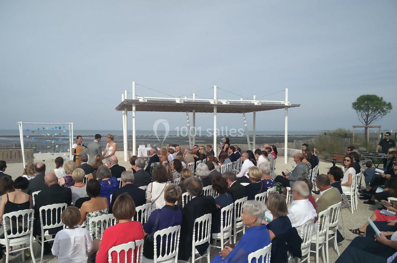 Cérémonie en plein air avec des invités assis sur des chaises blanches, face à un officiant près de la mer.