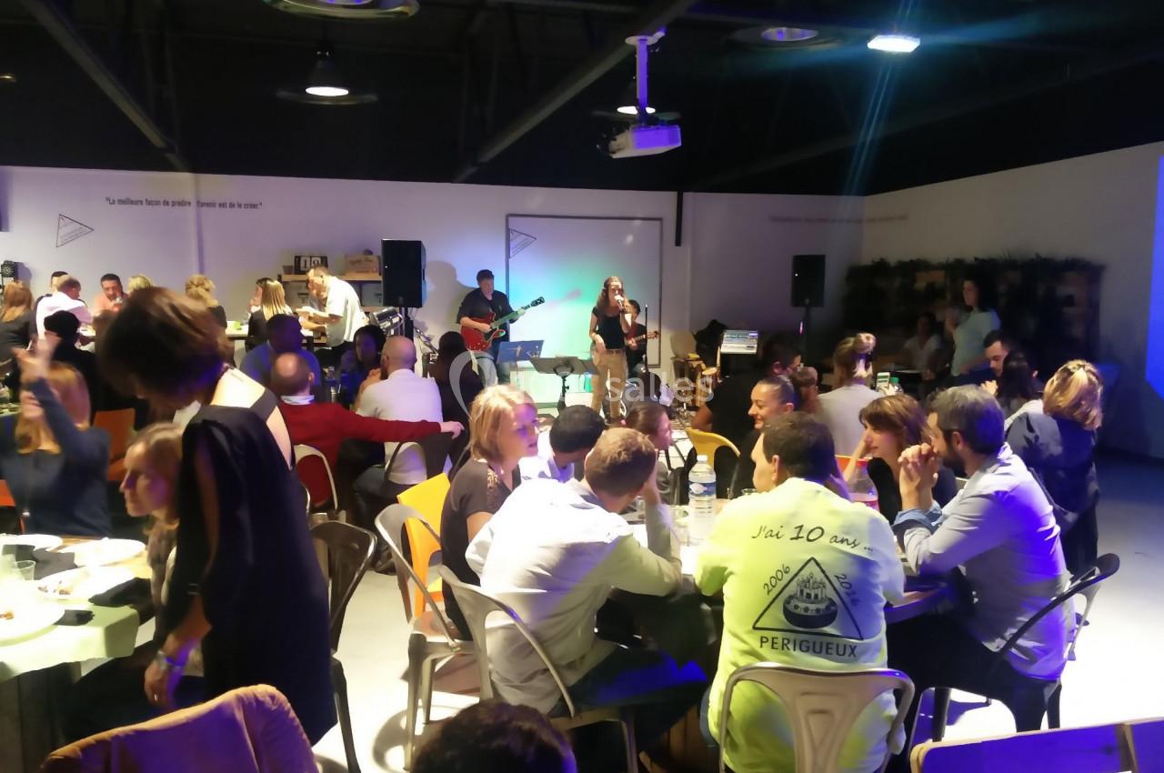 Des personnes dînent et discutent dans une salle animée avec un groupe de musique jouant en arrière-plan.