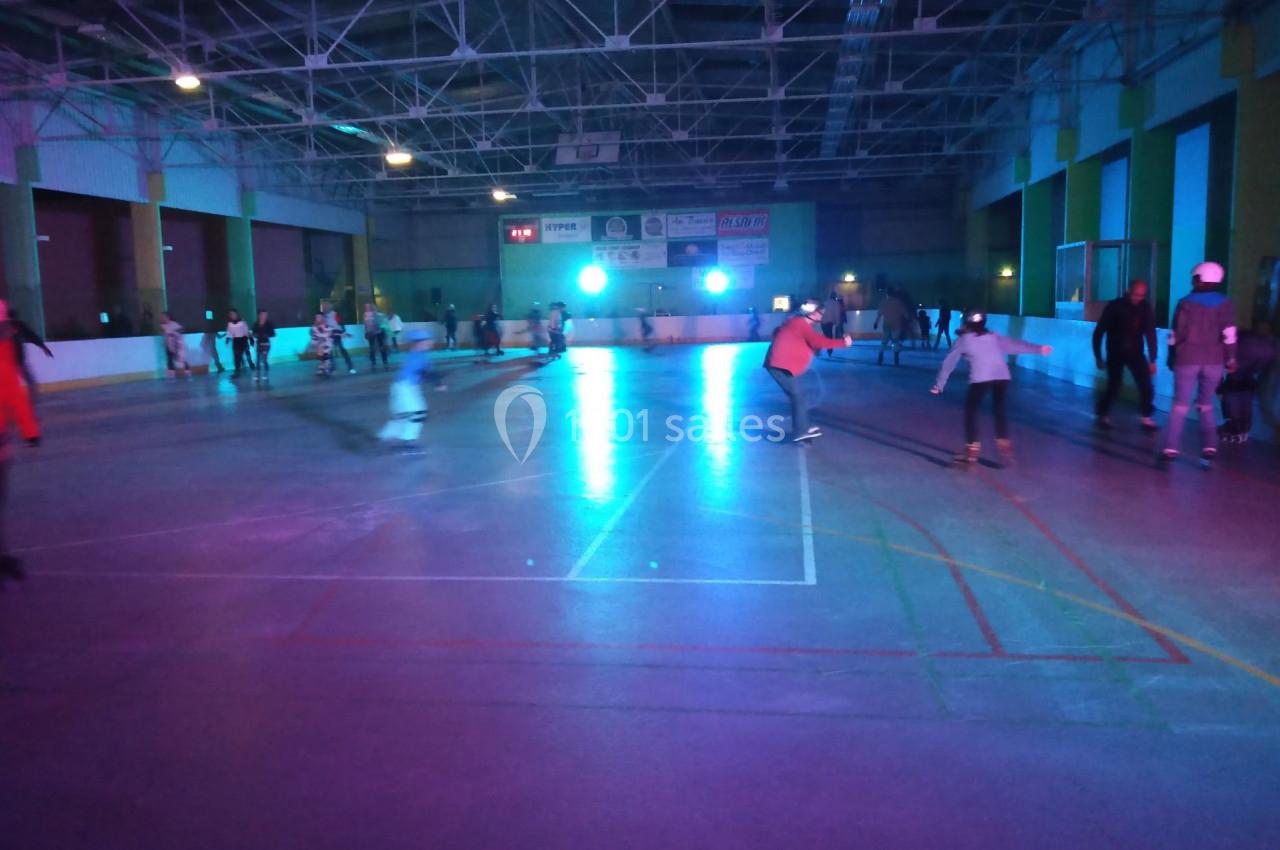 Personnes patinant dans une patinoire intérieure éclairée par des lumières colorées dans une ambiance nocturne.