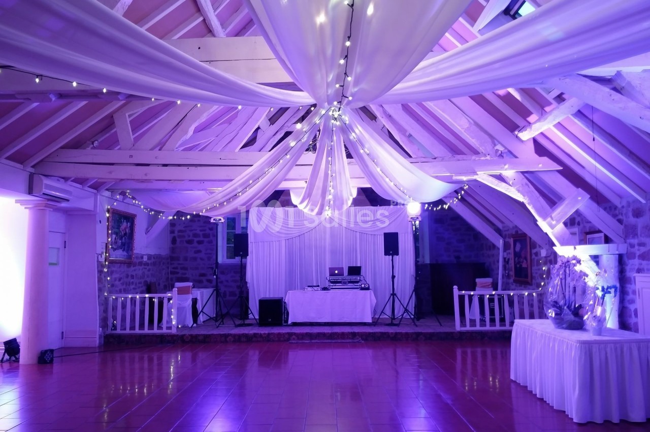Salle de réception avec charpente apparente, éclairage violet, décorations en tissu et équipements de sonorisation.