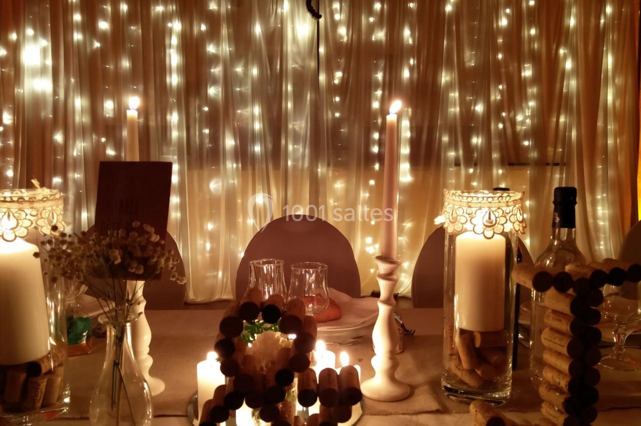 Table décorée avec des bougies, des guirlandes lumineuses et des éléments en liège, devant un rideau éclairé.