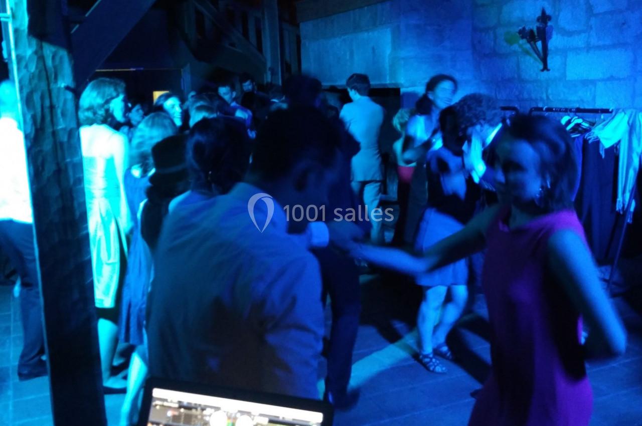 Personnes dansant dans une salle éclairée par des lumières bleues, avec un ordinateur de DJ au premier plan.