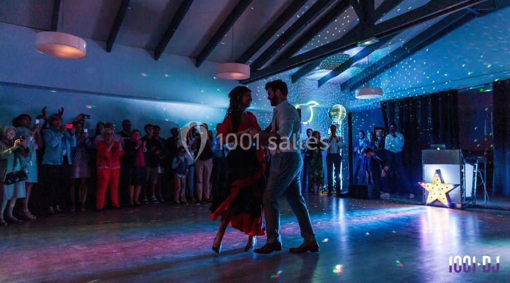 Un couple danse sur une piste éclairée par des lumières colorées, entouré de spectateurs dans une salle festive.