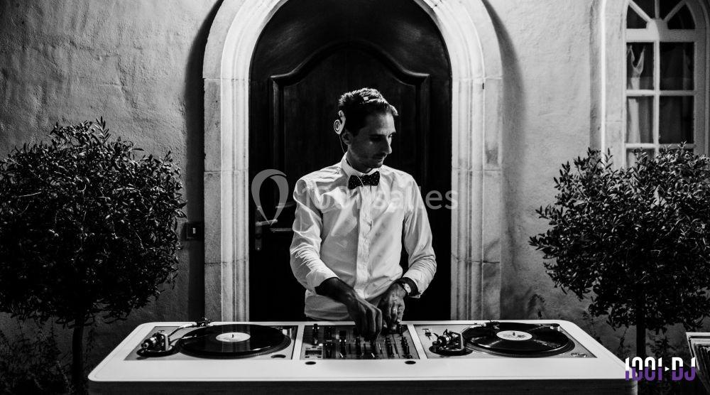 Un DJ en chemise et nœud papillon mixe de la musique sur une table de mixage entre deux platines vinyles.