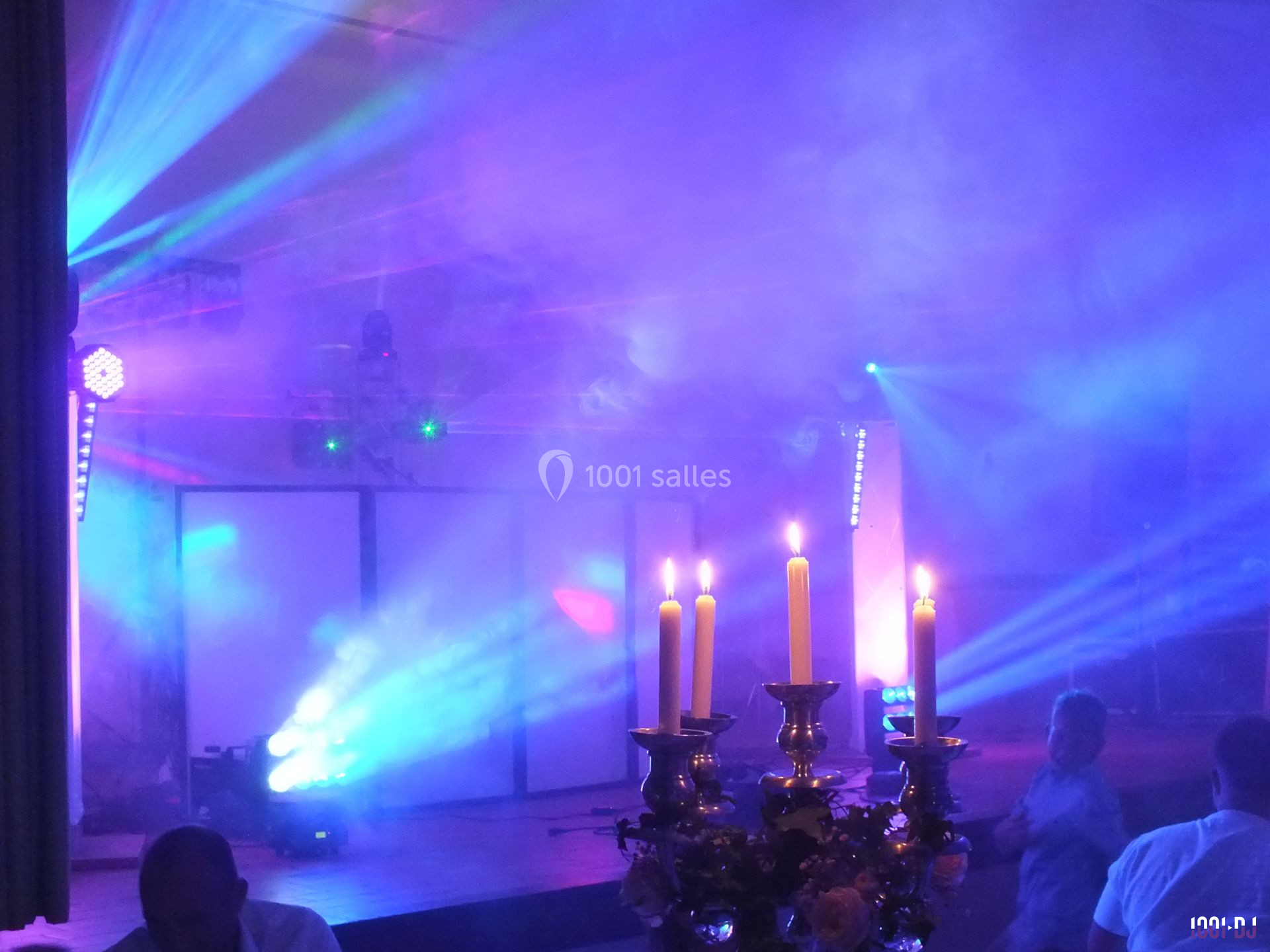 Salle de fête avec éclairages colorés, fumée et chandeliers allumés au premier plan.