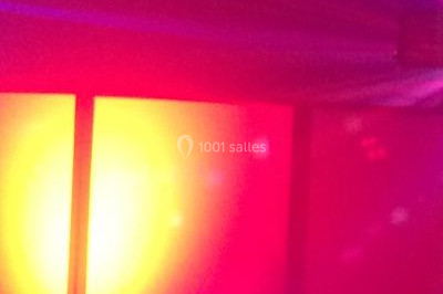 Façade en pierre éclairée par des lumières violettes et bleues, avec des tables en métal noir au premier plan.