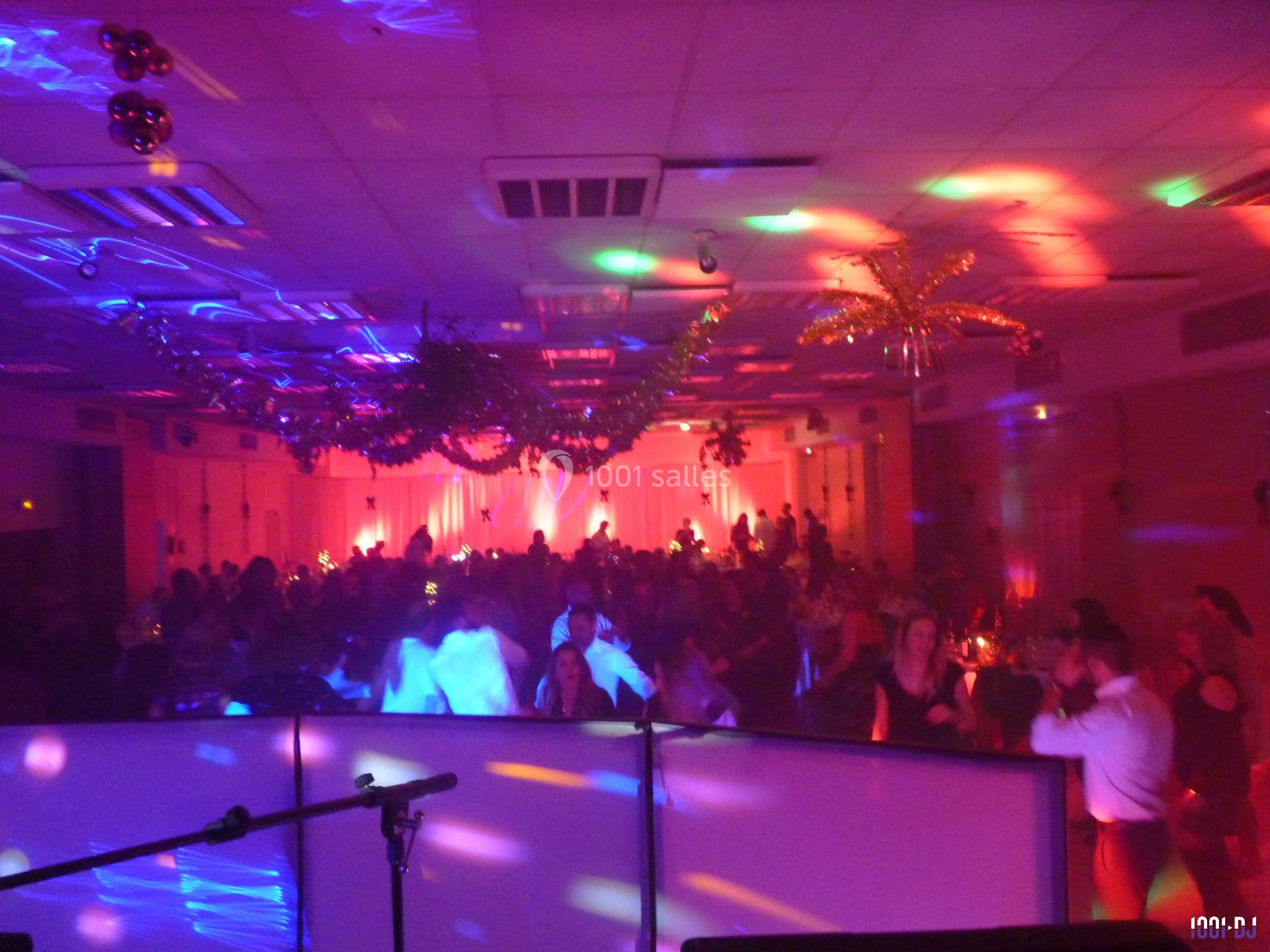 Salle de réception animée avec des invités dansant sous des lumières colorées et une décoration festive au plafond.