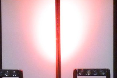 Façade en pierre éclairée par des lumières violettes et bleues, avec des tables en métal noir au premier plan.