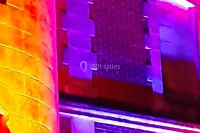 Façade en pierre éclairée par des lumières violettes et bleues, avec des tables en métal noir au premier plan.