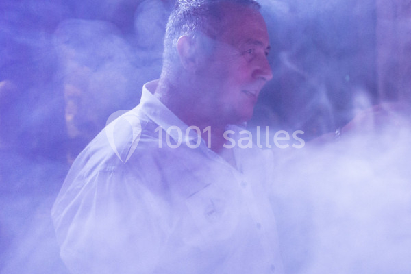 Homme en chemise blanche debout dans une ambiance enfumée et éclairée par une lumière violette.