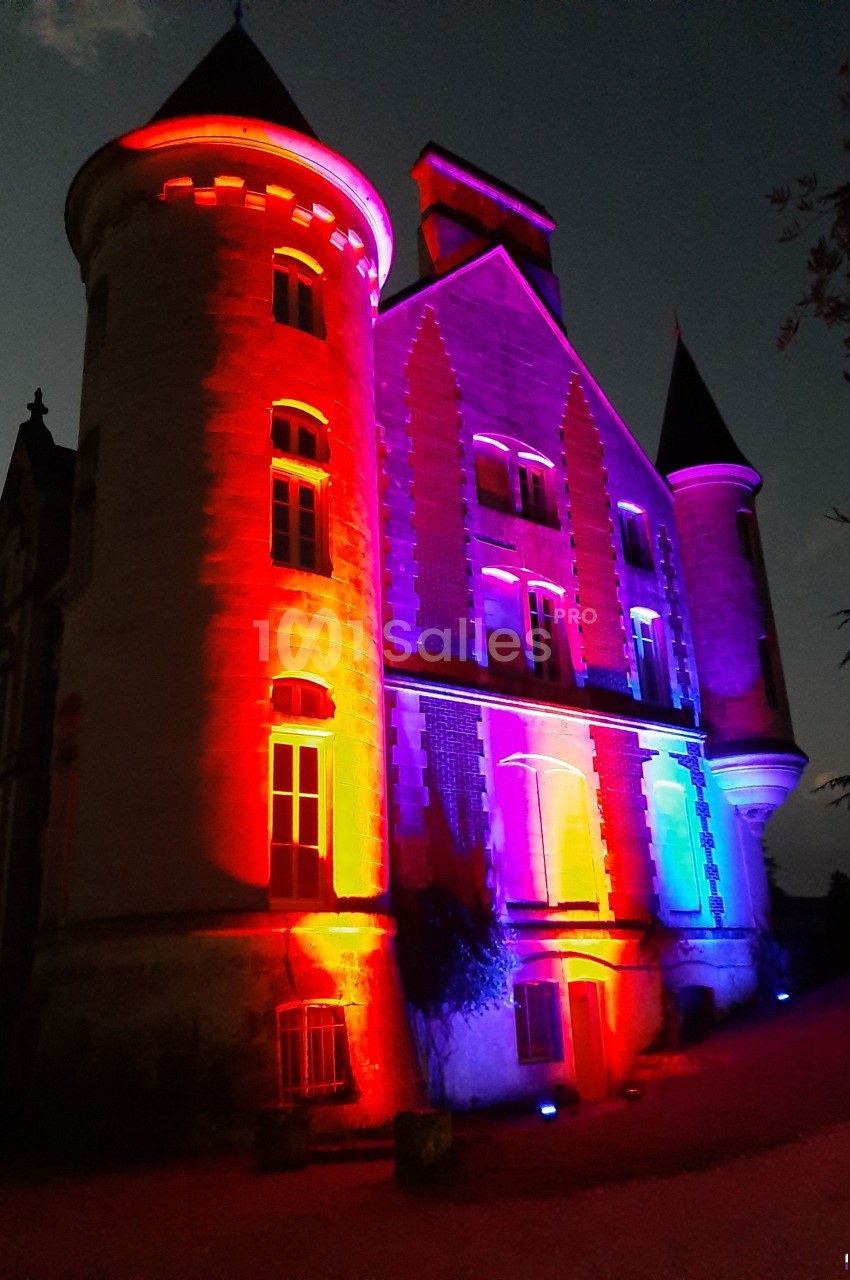 Façade d'un château éclairée par des lumières colorées rouges, bleues et violettes à la tombée de la nuit.