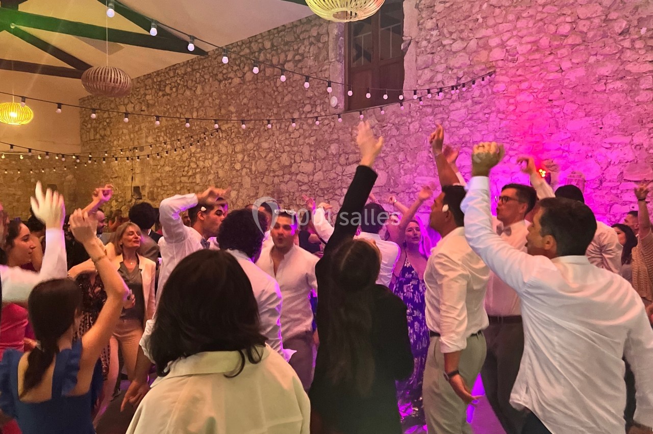 Personnes dansant et célébrant dans une salle en pierre éclairée par des guirlandes lumineuses et des lumières colorées.