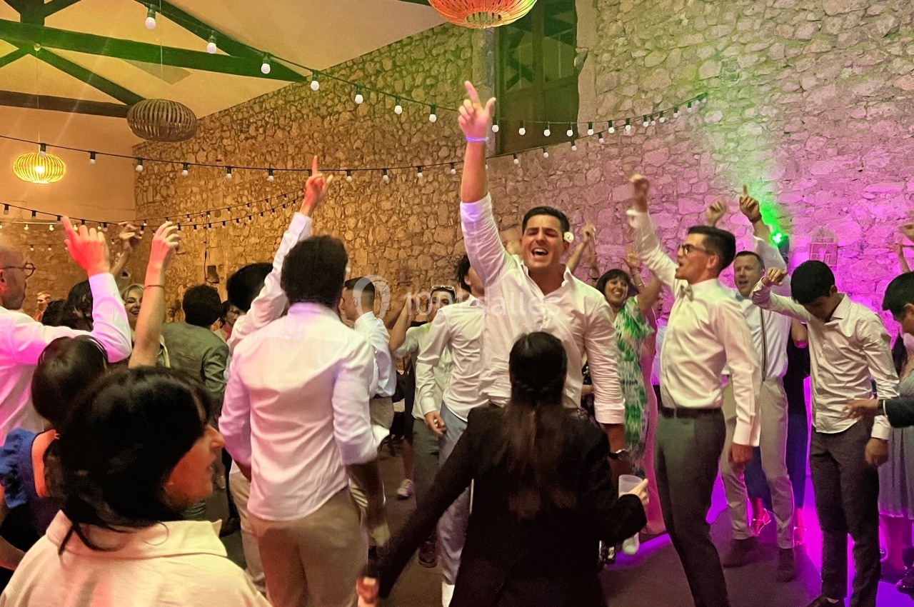 Des invités dansent et célèbrent dans une salle en pierre éclairée par des guirlandes lumineuses et des lampes suspendues.