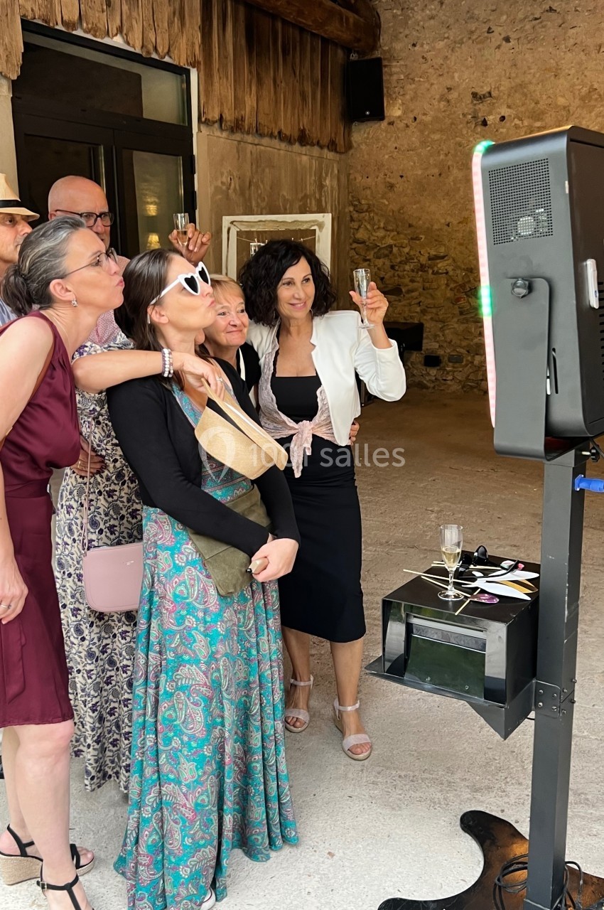 Des personnes posent ensemble devant une borne photo dans un espace en pierre, certaines tenant des verres.