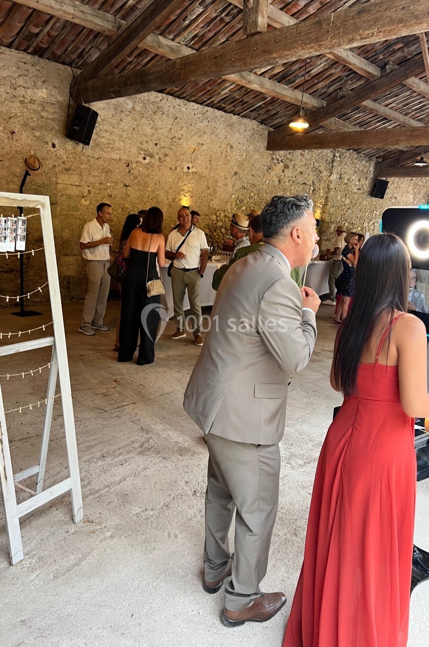 Des personnes discutent et utilisent une borne photo dans une salle en pierre avec un plafond en bois.