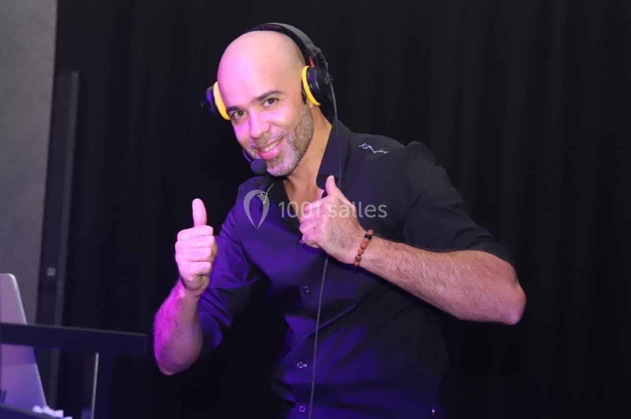 Homme souriant portant un casque audio, levant les pouces, devant un fond sombre.