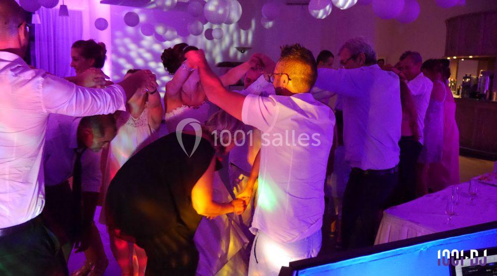 Des invités dansent ensemble dans une salle décorée de lumières colorées et de ballons suspendus.
