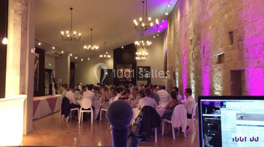 Salle de réception éclairée avec des invités assis à des tables rondes, vue depuis un micro en premier plan.