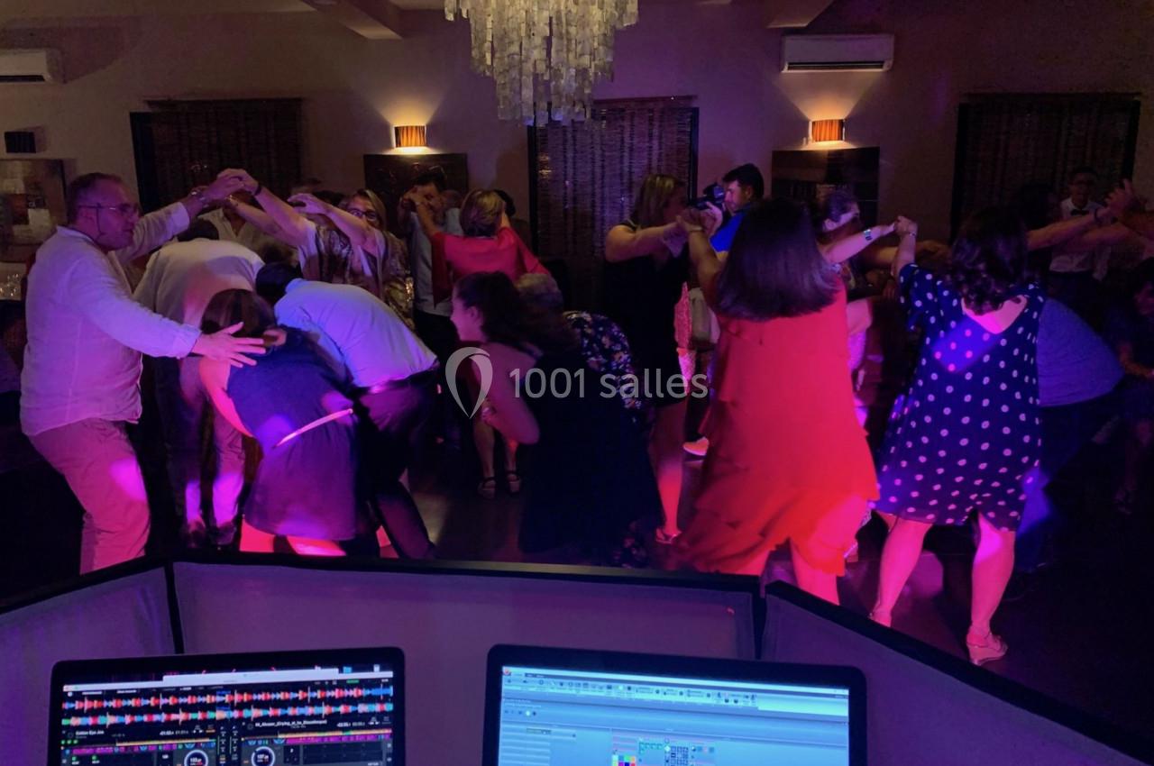 Des personnes dansent en cercle sous un éclairage coloré, vues depuis une table de mixage avec des écrans allumés.