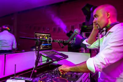 Deux hommes sur scène, l'un chante au micro tandis que l'autre pointe du doigt près d'un équipement audio.