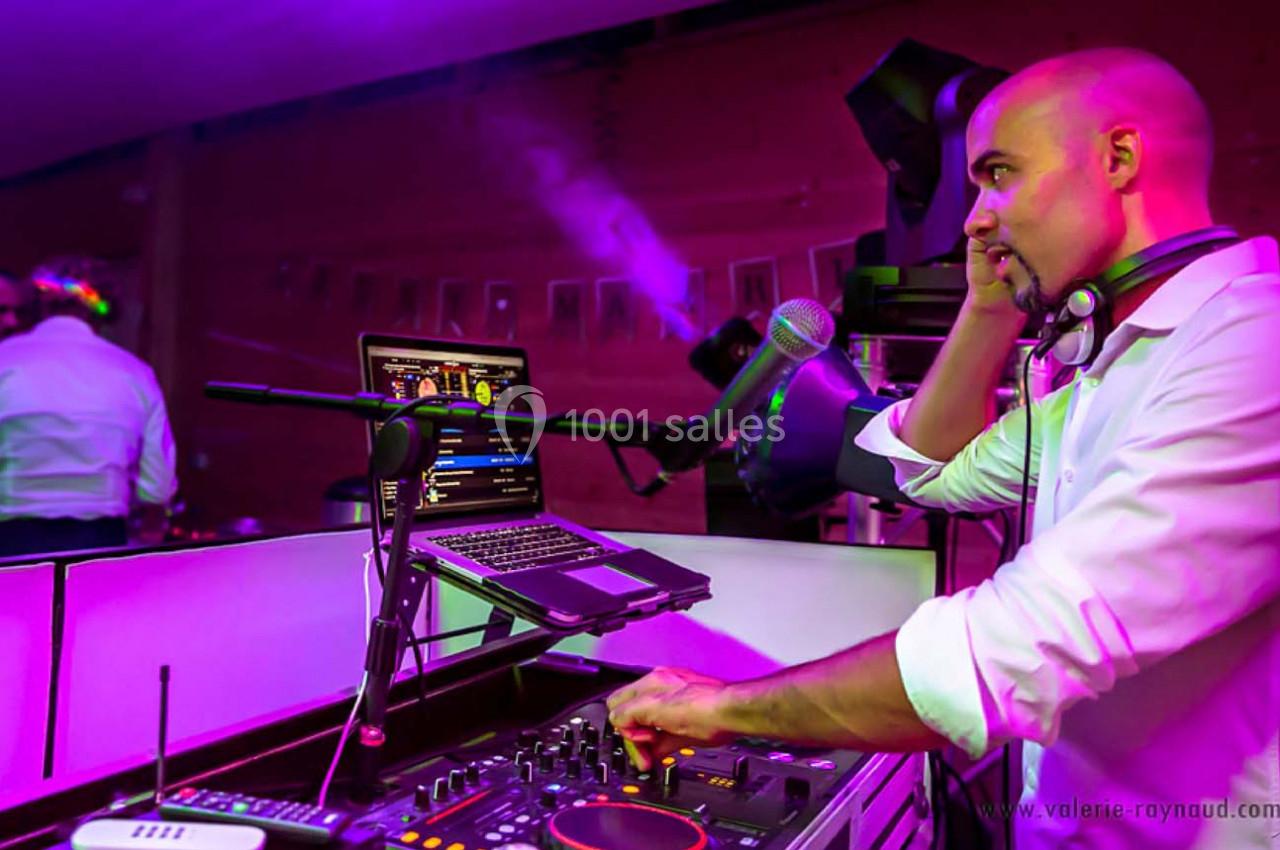 Un DJ mixe de la musique sur une console avec un ordinateur portable dans un environnement éclairé par des lumières colorées.