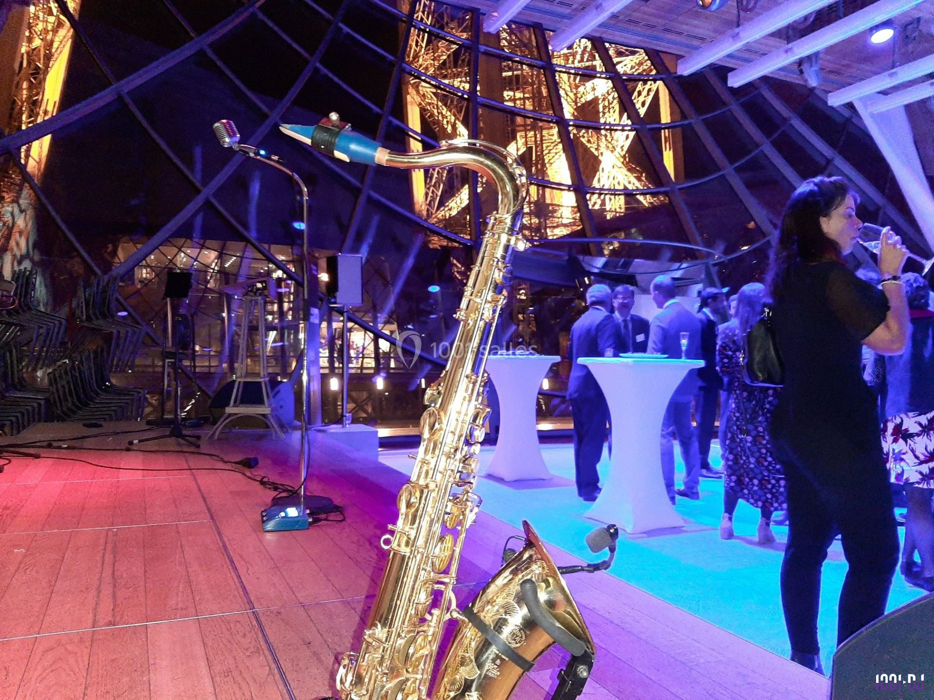 Un saxophone posé sur une scène en bois lors d'un événement avec des invités et une vue nocturne sur la Tour Eiffel.