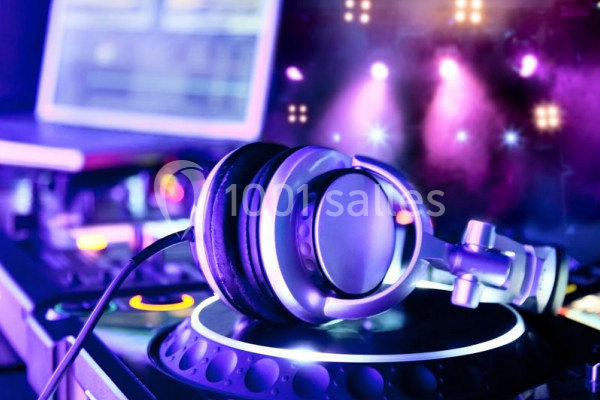 Casque audio posé sur une platine de DJ, avec des lumières colorées et un ordinateur en arrière-plan.