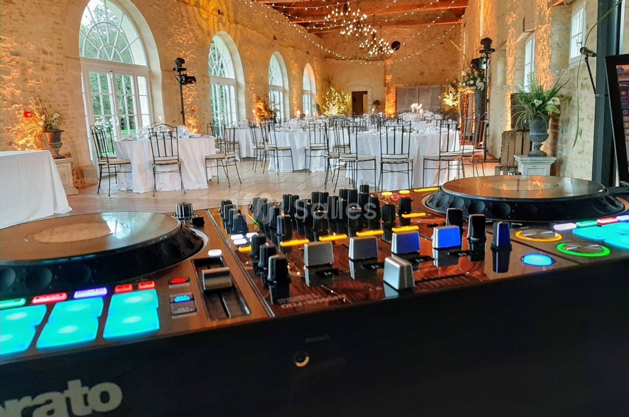 Vue d'une salle de réception élégante avec tables dressées, éclairages suspendus, et une table de mixage au premier plan.