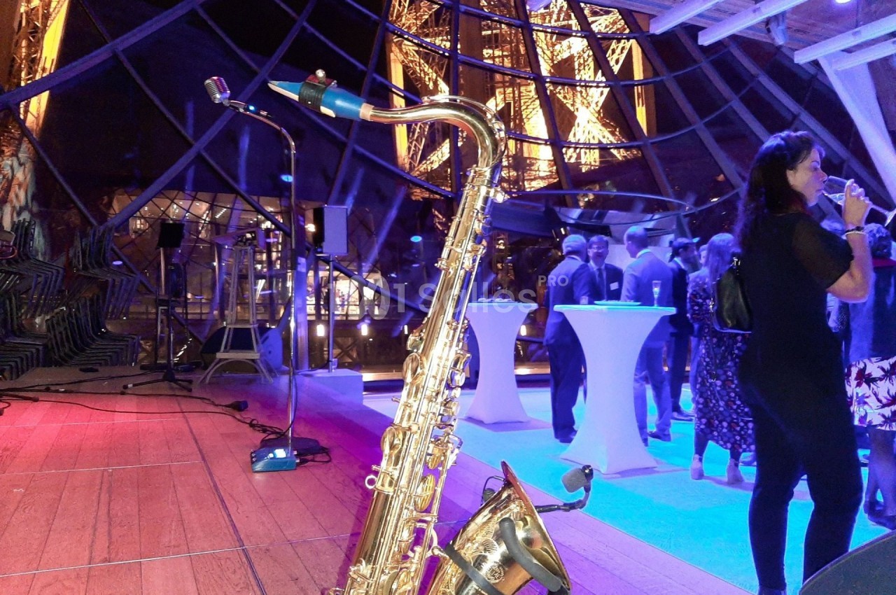 Un saxophone posé sur une scène en bois lors d'un événement avec des invités et une vue nocturne sur la Tour Eiffel.