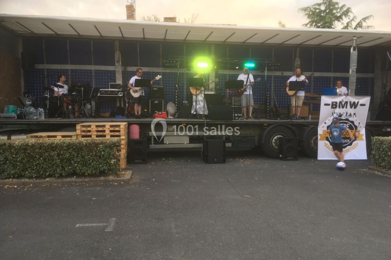 Un groupe de musiciens joue sur une scène extérieure équipée de lumières et d'instruments, devant un public absent.