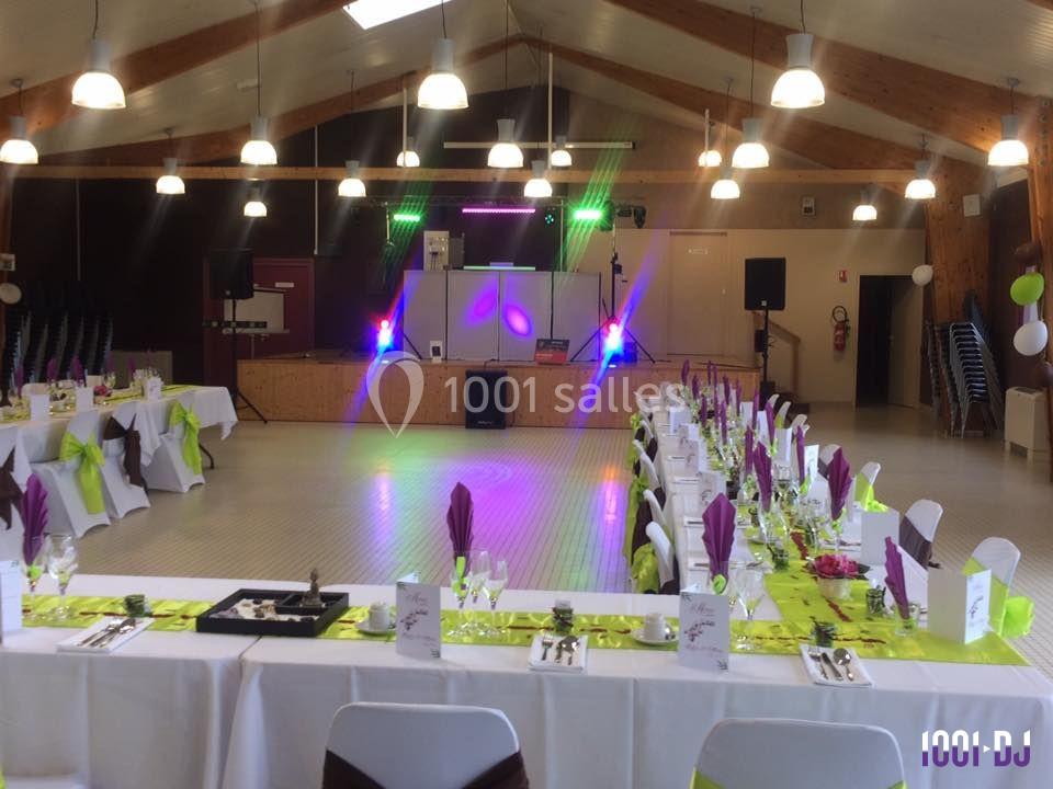 Salle de réception décorée avec des tables dressées en blanc, vert et violet, et une piste de danse éclairée.