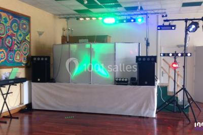 Salle décorée avec des tables dressées, des ballons et une scène équipée d'instruments de musique et de projecteurs.