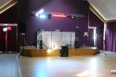 Salle décorée avec des tables dressées, des ballons et une scène équipée d'instruments de musique et de projecteurs.