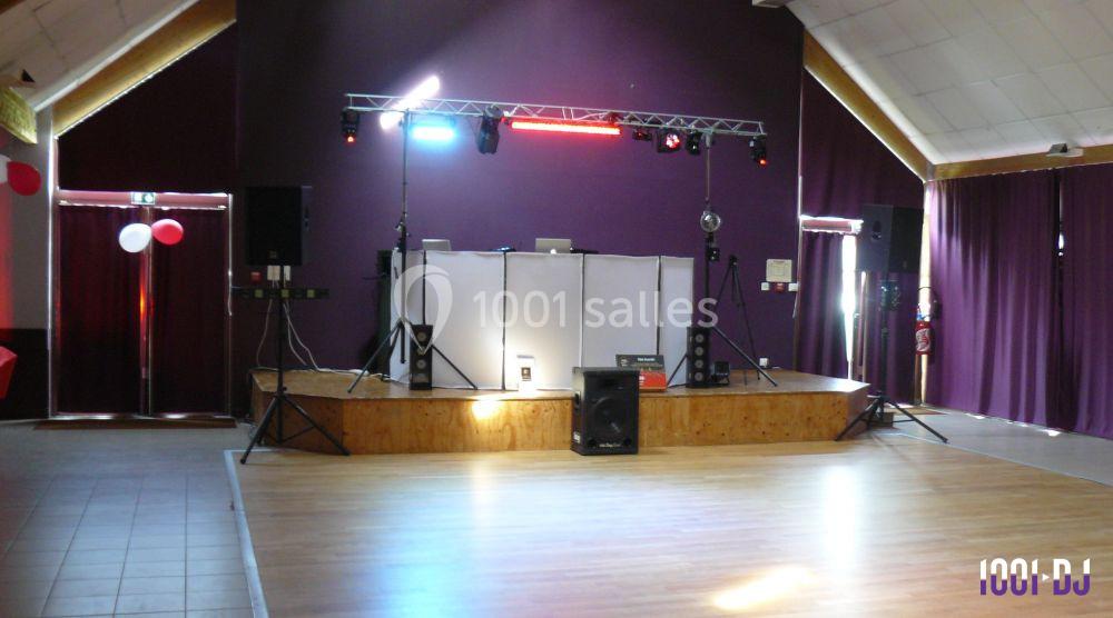 Scène équipée de matériel de sonorisation et d'éclairage dans une salle avec rideaux violets et parquet clair.