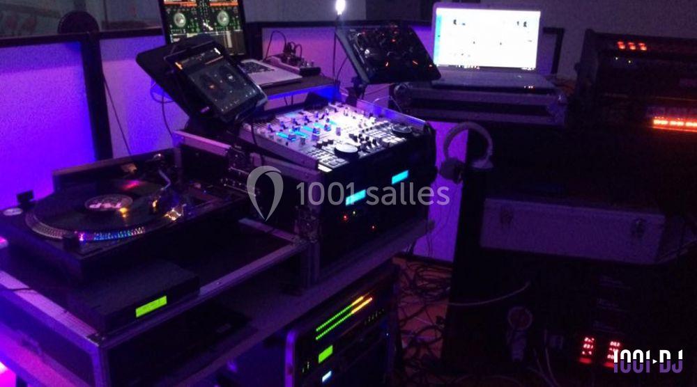 Équipement de DJ comprenant platines, table de mixage et ordinateurs dans un environnement éclairé par des lumières colorées.