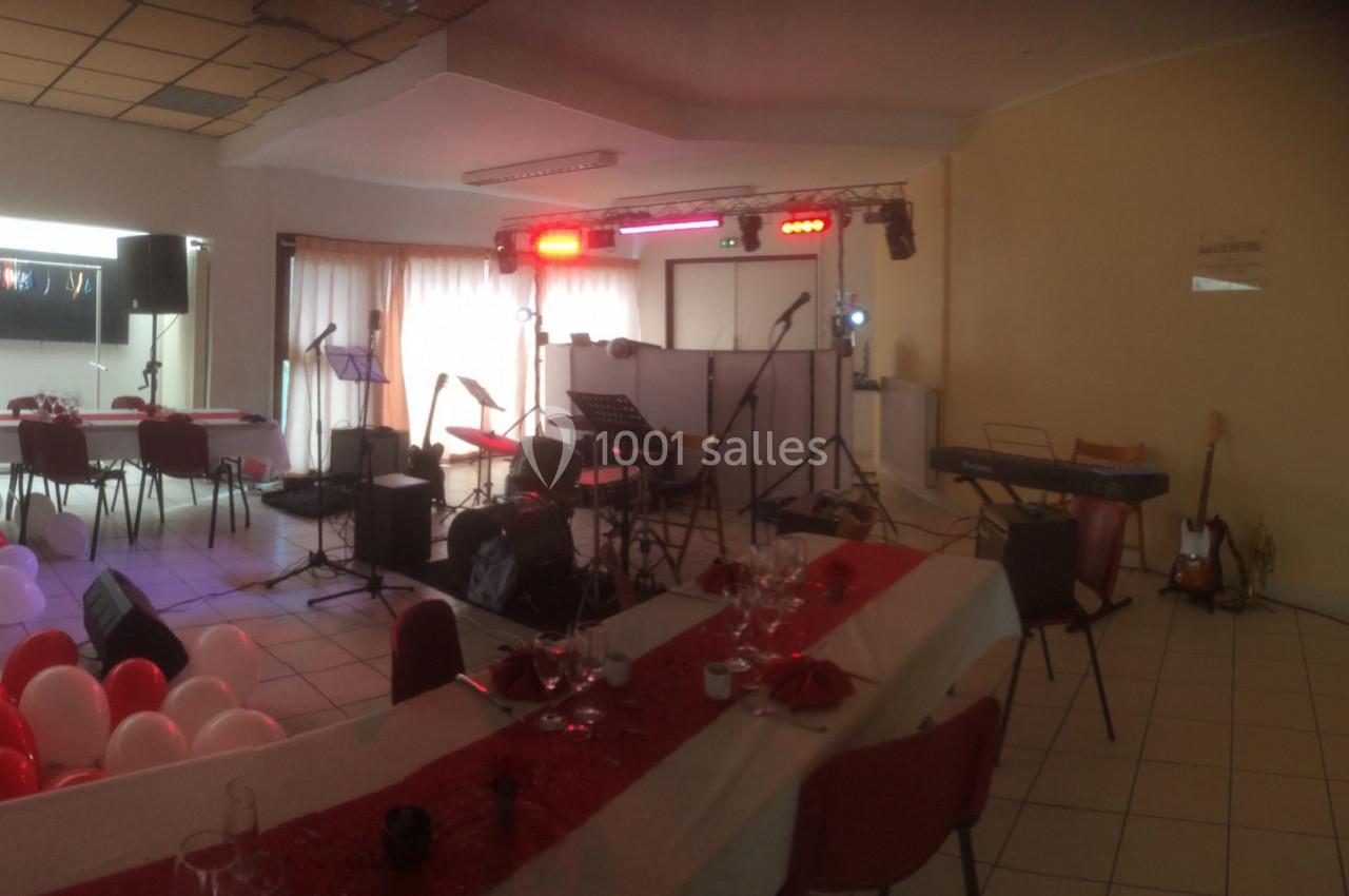 Salle décorée avec des tables dressées, des ballons et une scène équipée d'instruments de musique et de projecteurs.