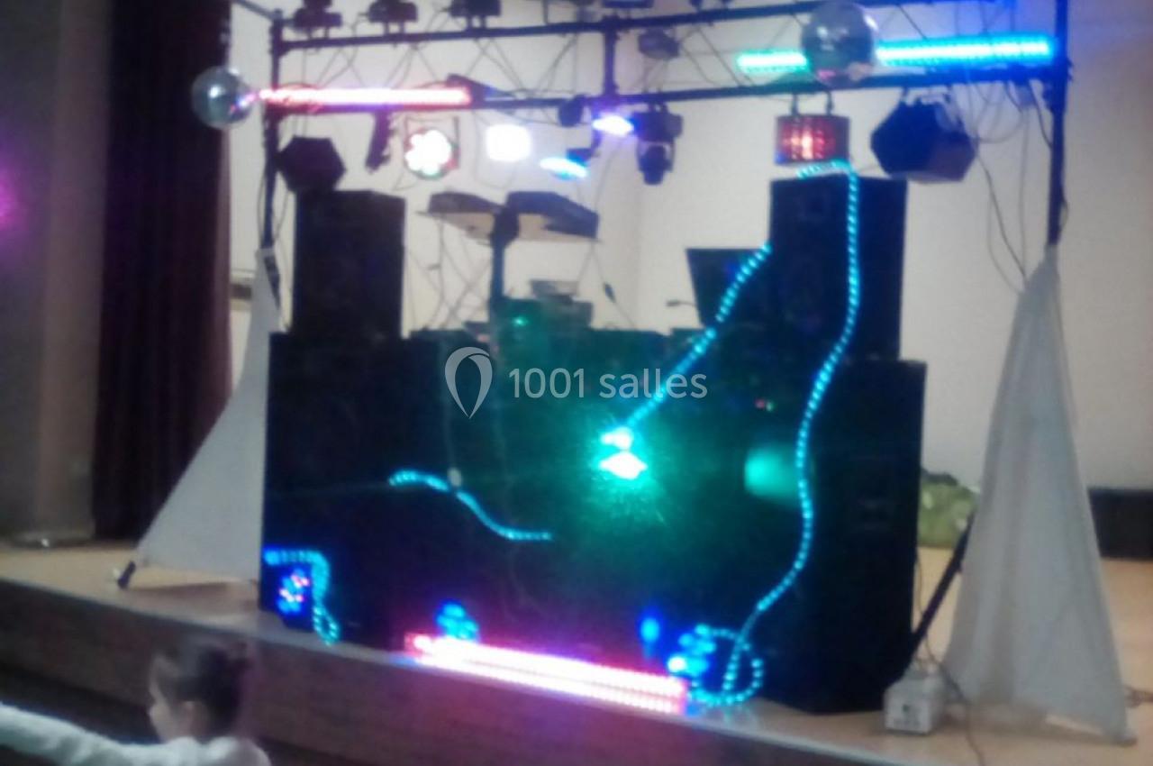 Installation de matériel de sonorisation et d'éclairage coloré sur une scène intérieure, avec des enfants au premier plan.