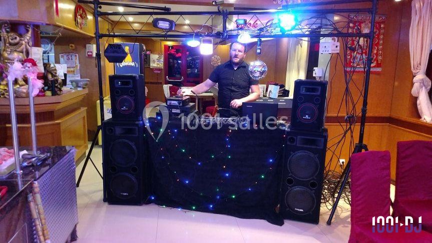 Un DJ debout derrière une table équipée de matériel audio et éclairages dans un espace intérieur décoré.