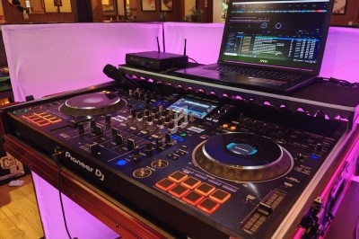 Un DJ mixant de la musique sur une table de mixage éclairée par des lumières colorées dans une ambiance nocturne.