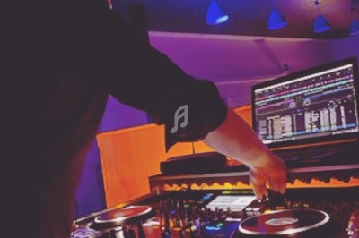 Un DJ mixant de la musique sur une table de mixage éclairée par des lumières colorées dans une ambiance nocturne.