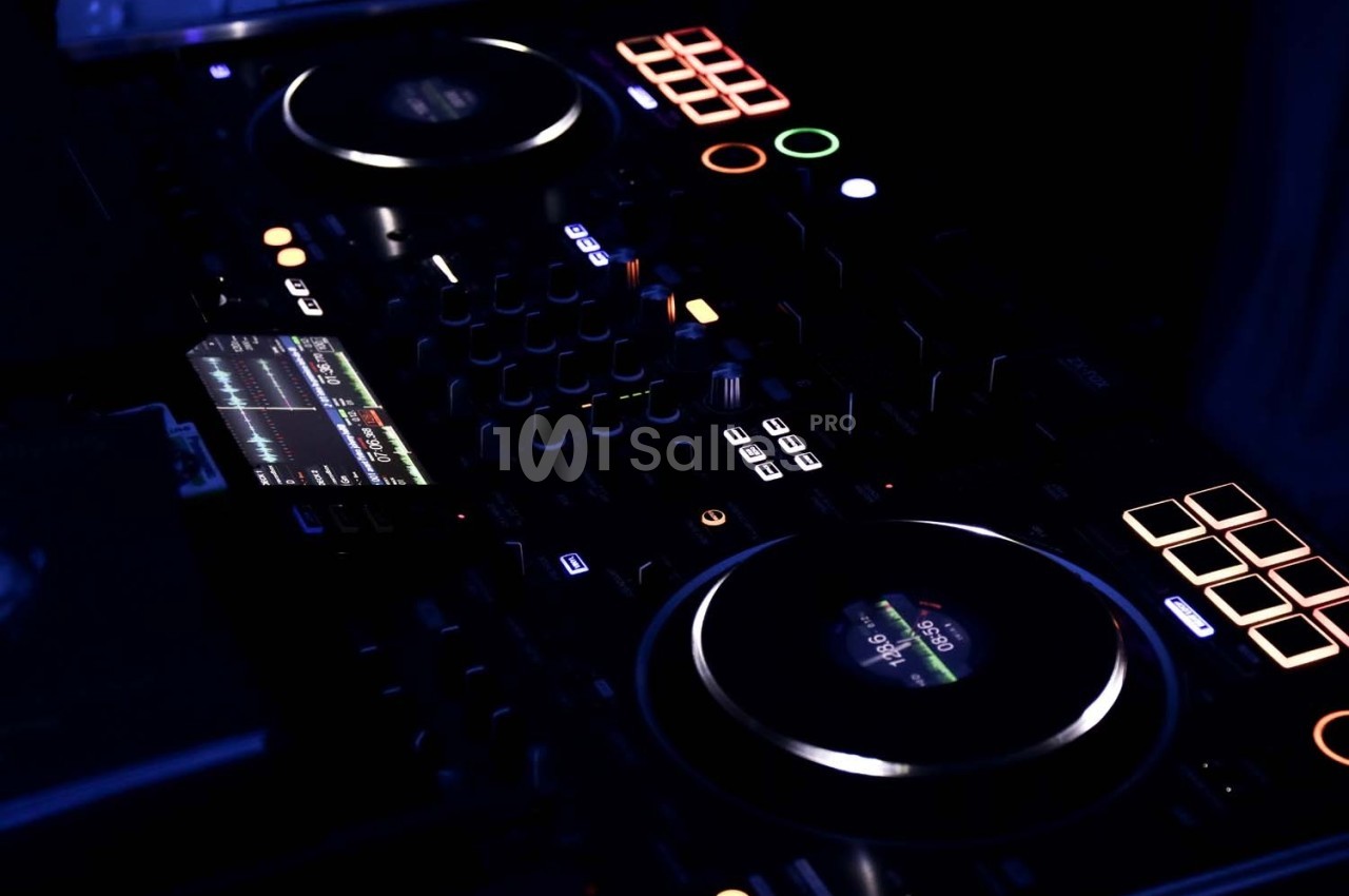 Console de mixage DJ éclairée dans un environnement sombre, avec boutons et écrans lumineux.