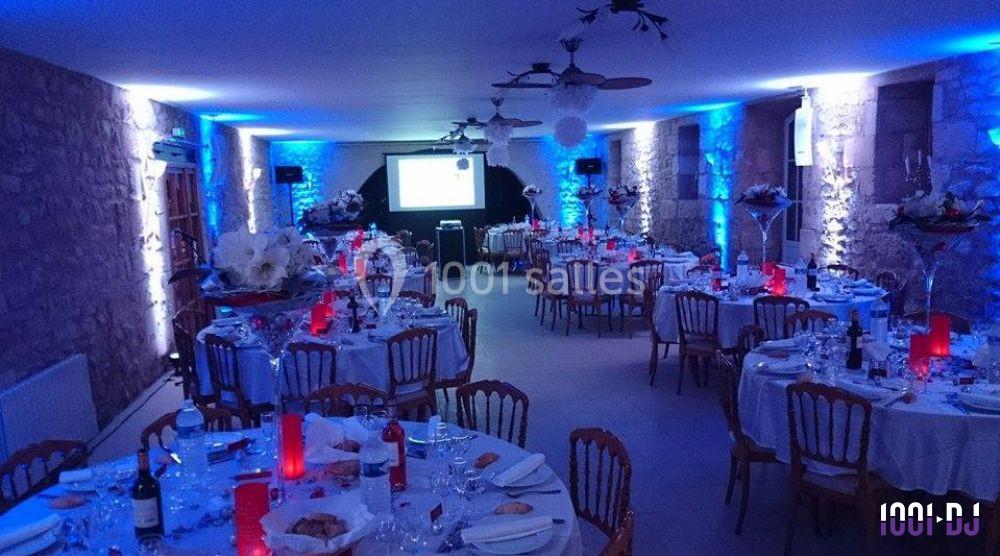Salle de réception décorée avec des tables rondes dressées, éclairage bleu et rouge, écran de projection au fond.
