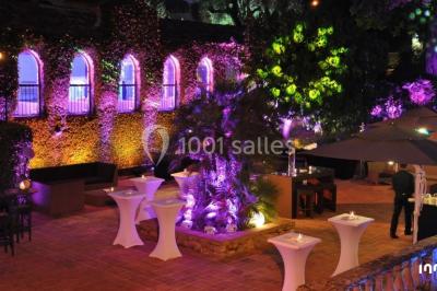 Salle de réception en plein air sous une verrière, avec tables décorées, nappes blanches et éclairage chaleureux.