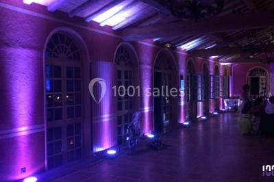 Salle de réception en plein air sous une verrière, avec tables décorées, nappes blanches et éclairage chaleureux.