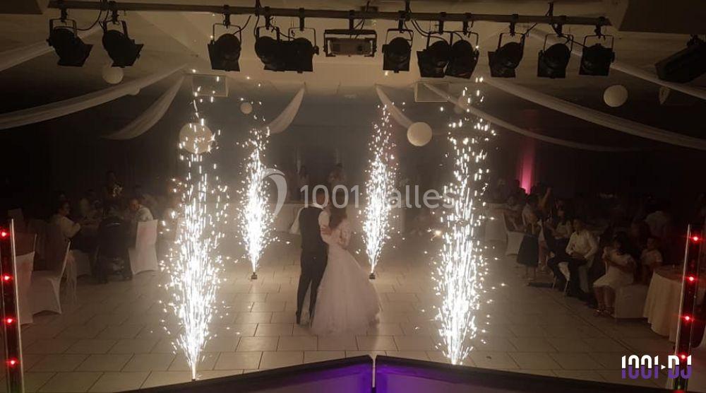 Un couple danse au centre d'une salle décorée, entouré de fontaines d'étincelles et d'invités assis.