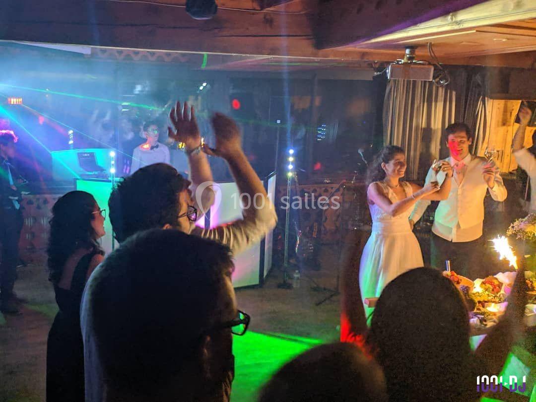 Des invités dansent et applaudissent sur une piste éclairée, tandis qu'un couple célèbre avec un gâteau.