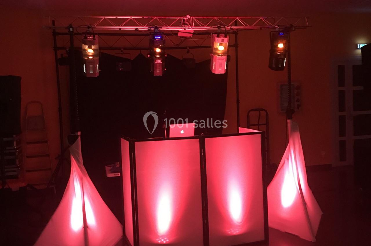 Pupitre de DJ éclairé par des lumières rouges et oranges, avec des structures lumineuses triangulaires autour.
