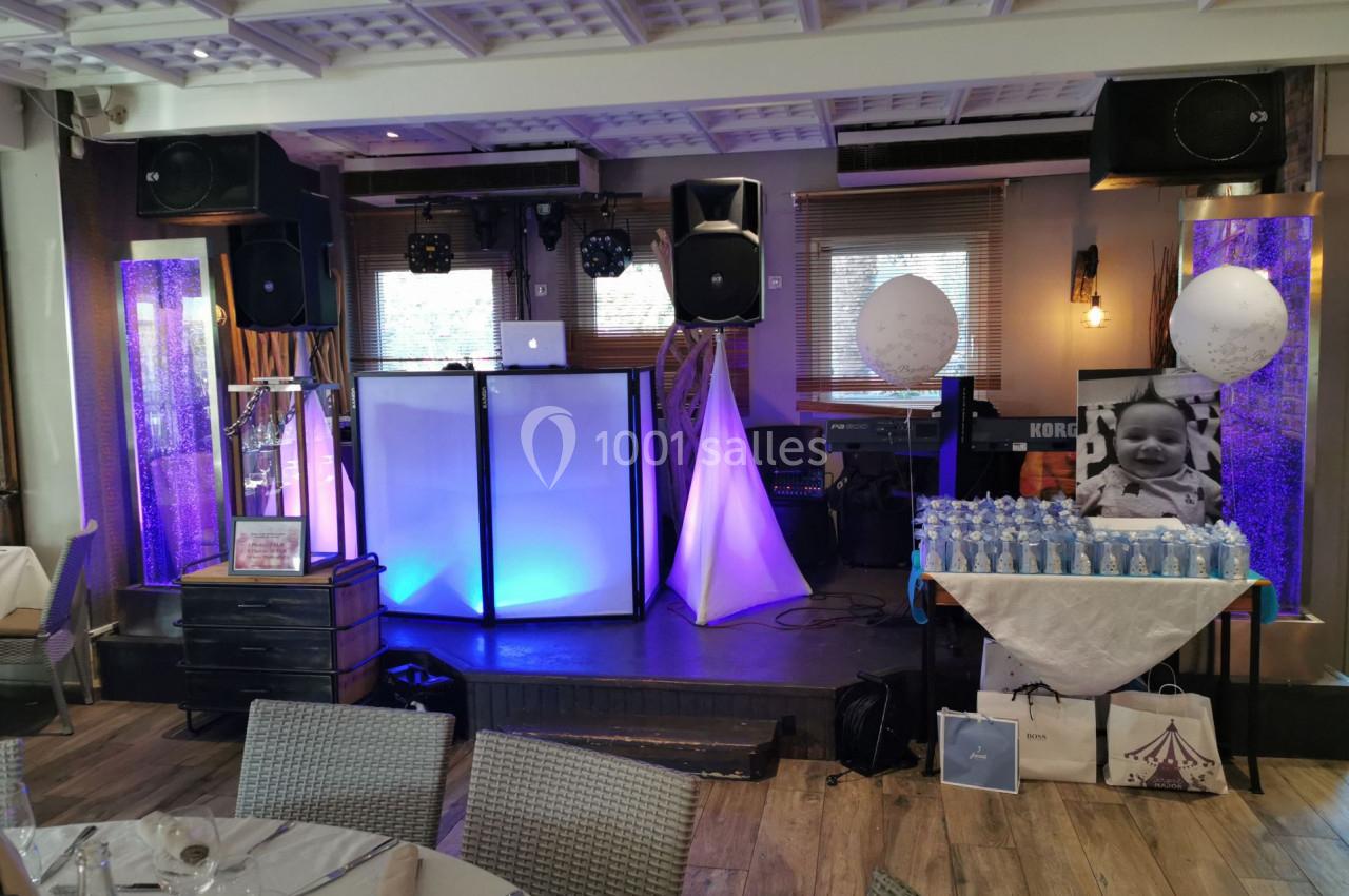 Salle décorée pour un événement avec une table de boissons, un stand DJ éclairé et des ballons décoratifs.