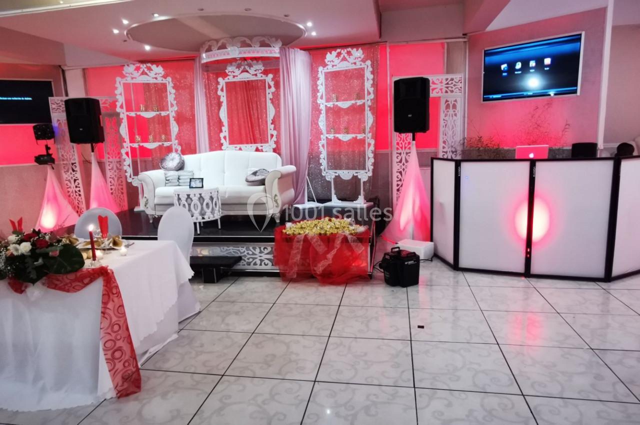 Salle de réception décorée en rouge et blanc avec une estrade, un canapé, une table ornée et un espace DJ.