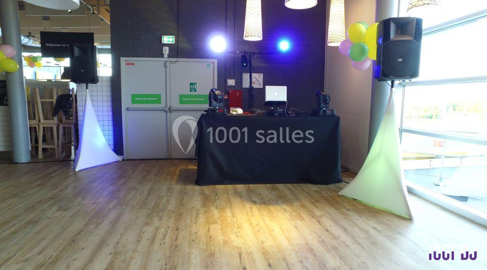 Table de mixage avec équipement audio et éclairage coloré dans une salle aux murs sombres et sol en bois clair.